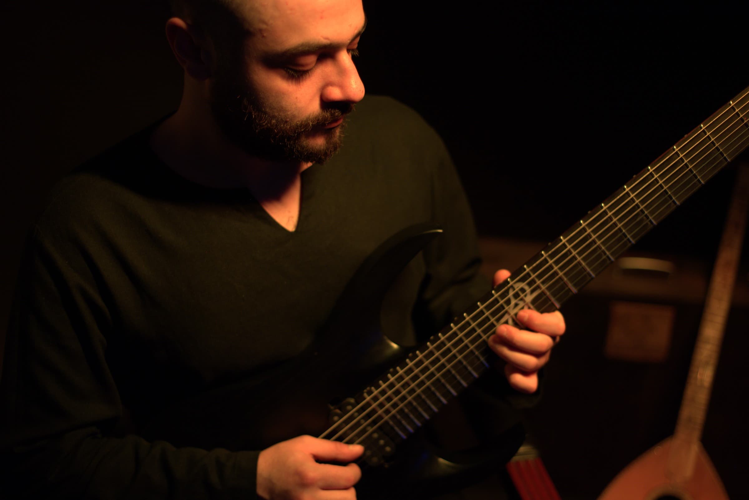 Youssef playing an electric guitar in warm, low light